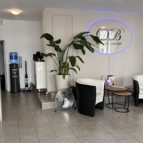 Leere  Lobby  mit  Logo  an  der  Wand,  weiße  Sessel,  grüne  Pflanze,  Ventilator